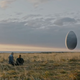 A couple watches a large egg floating on the horizon